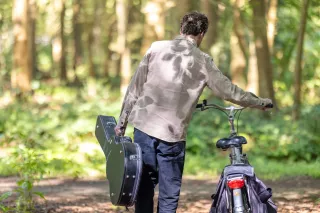 Vacatures - werken bij K&C - man loopt met gitaar en fiets in bos